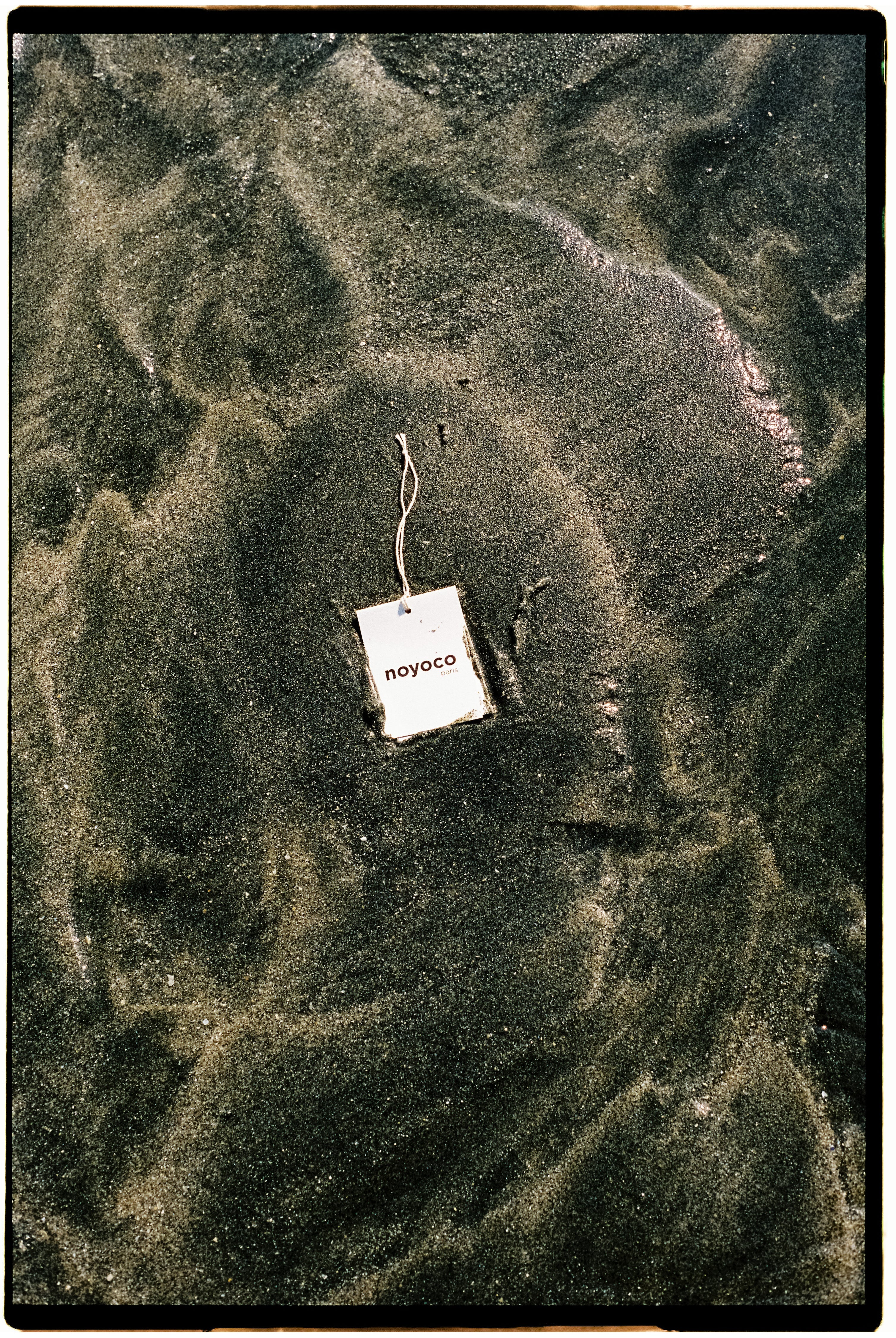 étiquette de vêtement noyoco dans le sable et l'eau d'une place en Normandie