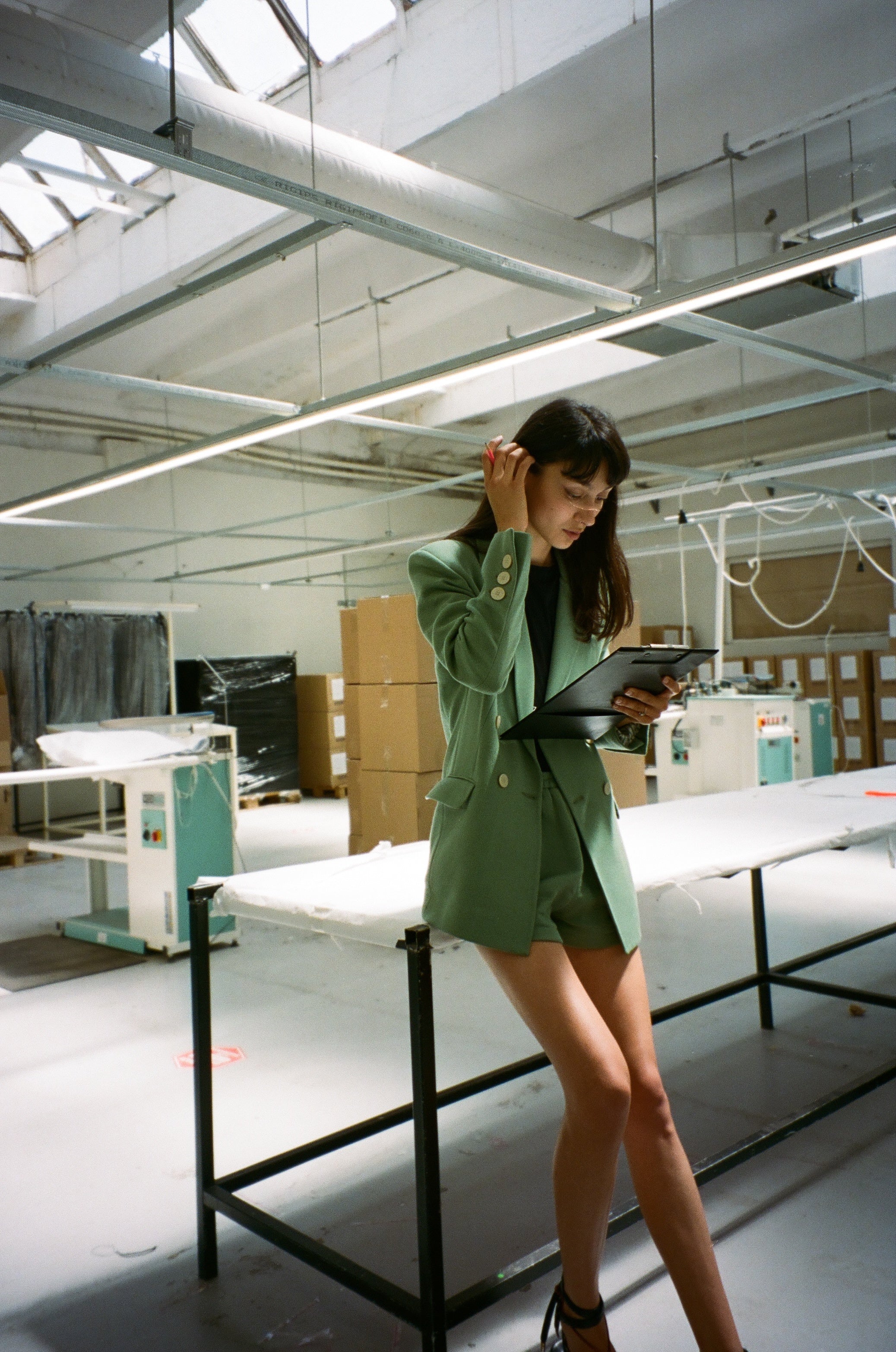 femme en veste de costume verte adossée à une table dans une usine de vêtement en Roumanie