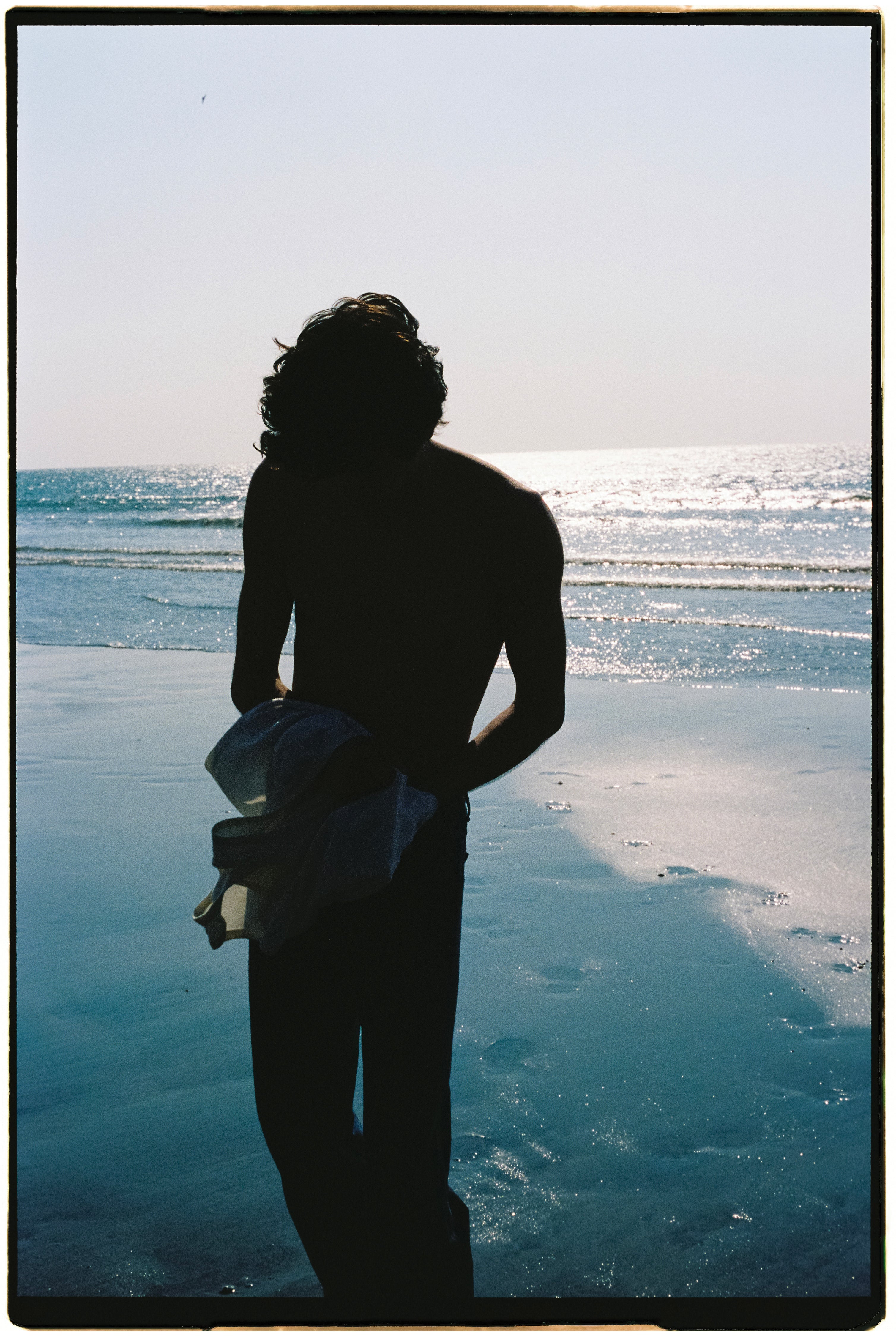 homme à contrejour sur une plage avec le reflet de l'eau bleue