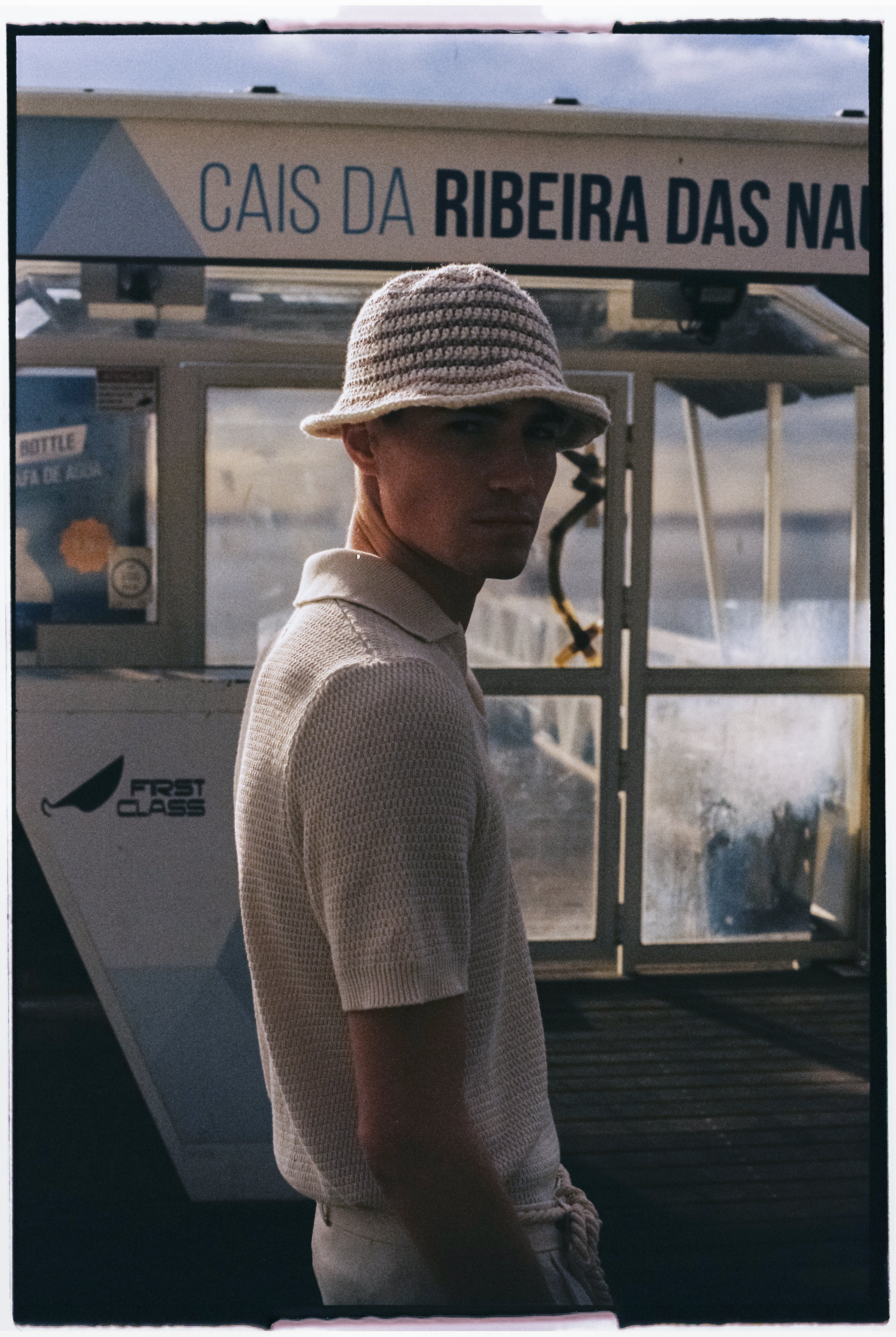 polo blanc en maille porté par un homme devant un bateau à Lisbonne