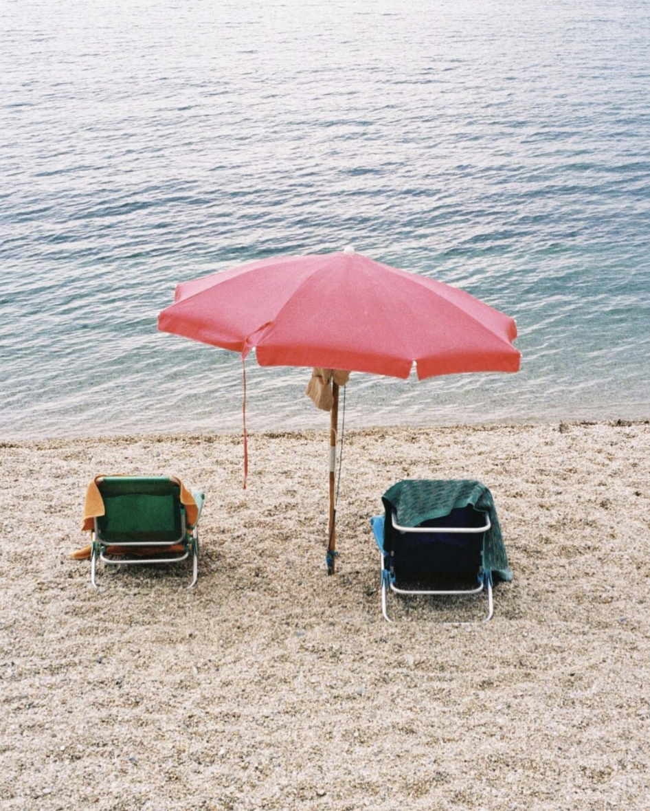 deux transats sous un parasol rose au bord de l'eau sur une plage dans le sud de la France