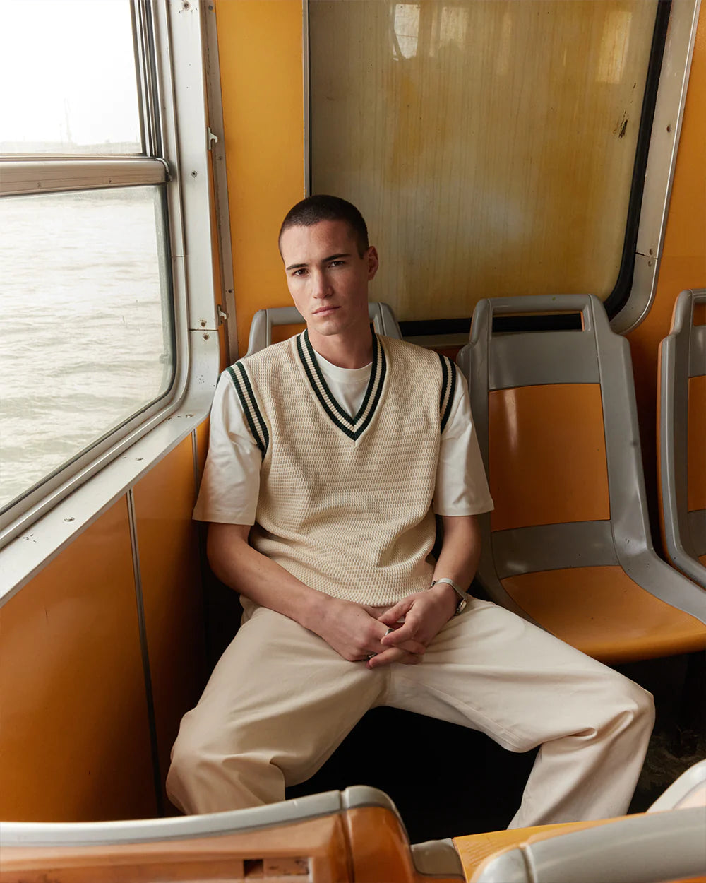 pull sans manches écru en mailles porté par un homme assis dans un ferry orange à Lisbonne