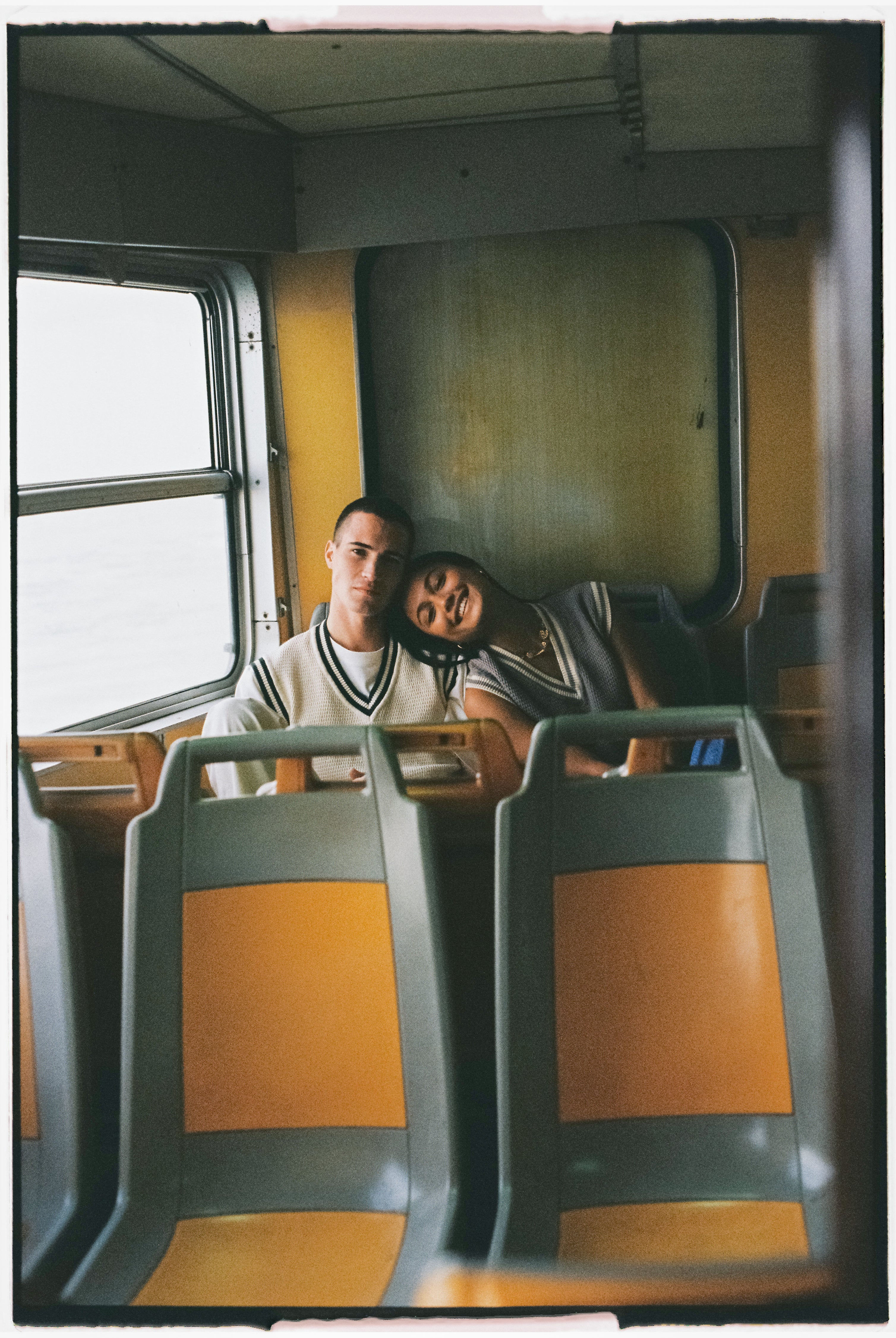 une femme posant sa tête sur l'épaule d'un homme dans un ferry à Lisbonne derriere des sièges orange